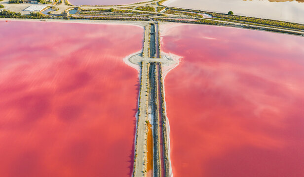 Aerial view of the vivid pink salt evaporation ponds and crystallized salt banks in the Camargue, featuring geometric saltworks and industrial production in Aigues-Mortes, Occitanie, France.