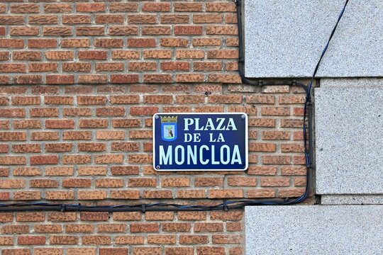 A traditional blue metal sign with the name of the Moncloa Square and the coat of arms of Madrid, Spain, mounted on the brick wall of a historic building in the capital of Spain. August 28, 2026