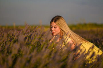 Obraz premium Beautiful young girl posing in lavender field. A bright yellow dress with a soft, flowing fabric set against a background of blooming purple lavender