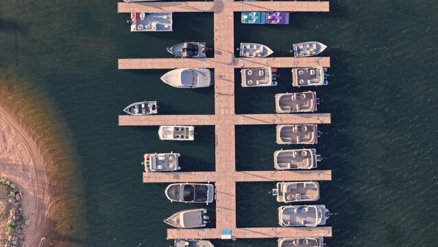 Aerial view of the marina at Lake Estes with various boats docked at wooden piers, surrounded by calm water and a sandy shoreline in Estes Park, Colorado, United States.