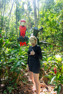 Woman standing on a forest trail beside a red parrot sculpture