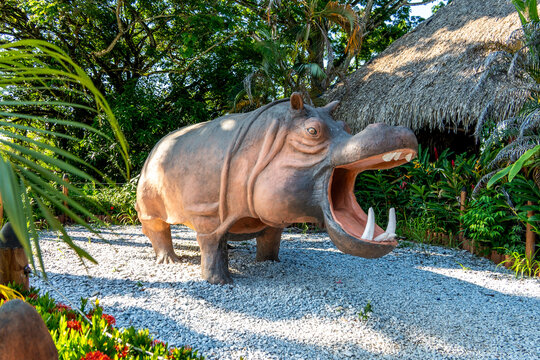 Hippo statue in tropical garden beside thatched hut