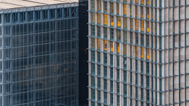 Aerial view of the modern glass and stone facades of the EUR district buildings, showcasing geometric architectural patterns and warm interior lighting in the evening Rome, Lazio, Italy.