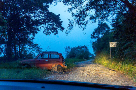 Red car on a rugged dirt road in a forest at blue hour