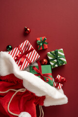 Naklejka premium Merry Christmas and Happy New Year Santa presents spilling from red velvet sack with ribbons on vertical burgundy table