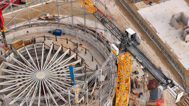 Aerial view of a large circular construction site featuring a radial steel framework, a yellow tower crane, and concrete foundations, Milan, Lombardy, Italy.