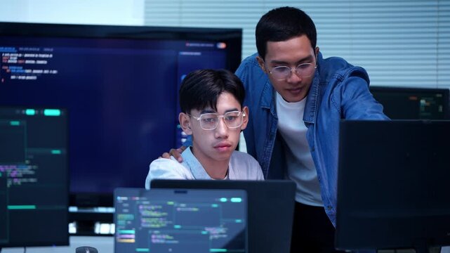 Two programmers collaborating in modern tech environment analyzing data on computer screens with code displayed