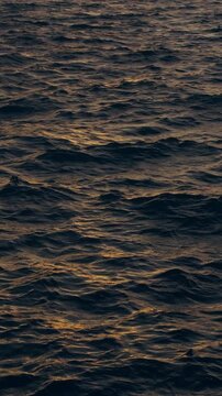 Vertical. Dark Ocean Waves Ripple Beneath Golden Sunset Reflections, Creating a Dramatic Natural Water Surface and Serene Coastal Atmosphere Vertical video.
