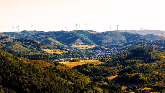Aerial view of the town of Bad Laasphe nestled in a valley surrounded by dense forests and rolling hills, with wind turbines on the ridges in Bad Laasphe, North Rhine-Westphalia, Germany.