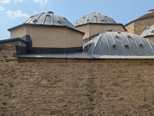 An artistic and atmospheric view looking up at majestic Ottoman hammam domes. The weathered textures of the historical rooftops contrast beautifully with a dramatic, colorful sunset sky. Light streams © kamchoo