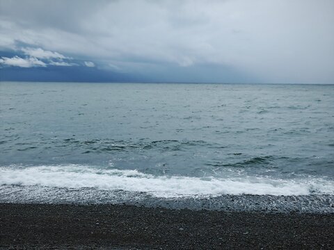 Turbulent ocean waves crashing on a dark pebble beach. Stormy weather and overcast sky over the sea