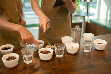 Coffee professionals evaluating brewed samples during a cupping session, with tasting cups, water...