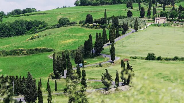 Van drive on winding cypress lined road through rolling hills in Tuscany, Italy