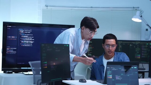 Collaborative programming session in modern it office with two developers analyzing code on multiple screens