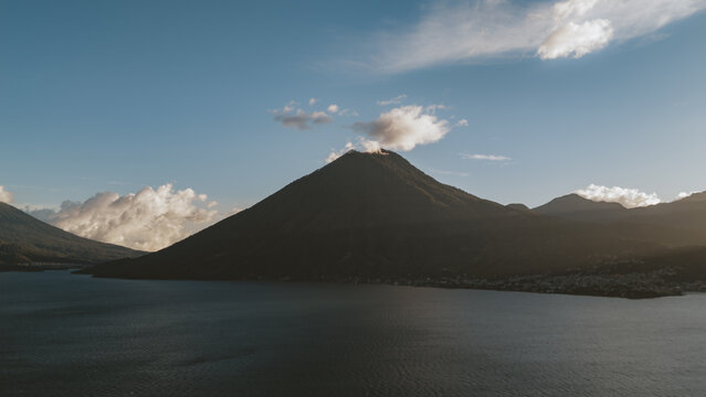 Aerial view of Lake Atitlan and its surrounding volcano under a clear blue sky with scattered clouds in Solola Department, Guatemala.