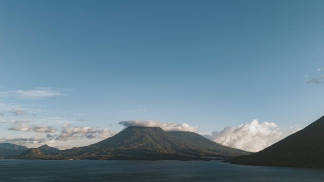 Aerial view of Lake Atitlan with its iconic volcanoes rising above the water under a clear blue sky in Solola Department, Guatemala.