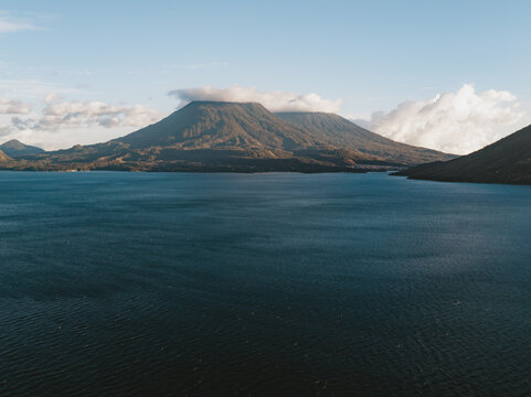 Aerial view of Lake Atitlan with its iconic volcanoes rising above the deep blue water under a clear sky in Solola Department, Guatemala.