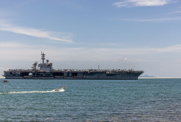 US Navy aircraft carrier USS Abraham Lincoln CVN 72 is anchored at sea. Military jets are parked on USS Abraham Lincoln. Small boat passes near USS Abraham Lincoln. © Nutchanart
