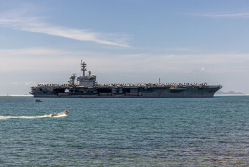 US Navy aircraft carrier USS Abraham Lincoln CVN 72 is anchored at sea. Military jets are parked on USS Abraham Lincoln. Small boat passes near USS Abraham Lincoln. © Nutchanart