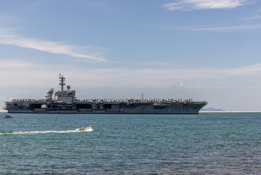 US Navy aircraft carrier USS Abraham Lincoln CVN 72 is anchored at sea. Military jets are parked on USS Abraham Lincoln. Small boat passes near USS Abraham Lincoln.