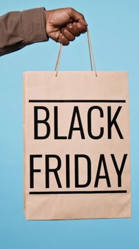 Vertical video of anonymous man holding paper shopping bag with Black Friday text against blue background. Clip suitable for retail sale campaigns, discount promos, and holiday marketing