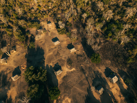 Aerial view of traditional thatched-roof huts scattered among ancient baobab trees in the dry landscape of the Avenue of the Baobabs in Morondava, Menabe, Madagascar.