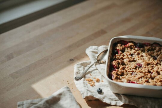 Baked berry crumble in a square white dish beside a crumpled linen napkin