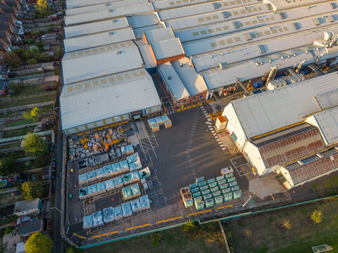 Aerial view of an industrial facility with large warehouse buildings, storage yards filled with palletized goods, and surrounding residential houses in Stafford, England, United Kingdom.