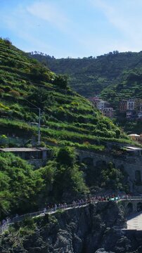 Scenic Trail in Cinque Terre with View of Hillside village Manarola and walking tourists people, aerial shot, vertical video