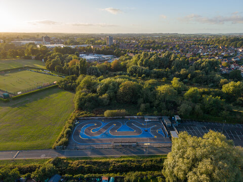 Aerial view of a remote controlled car track with a blue asphalt surface surrounded by lush green trees and a soccer field in Stafford, England, United Kingdom.
