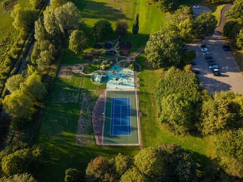 Aerial view of Wildwood Park featuring a tennis court, a playground, lush green trees, and a parking lot in Stafford, England, United Kingdom.