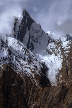 Aerial view of Uli Biaho Tower, a dramatic granite monolith mountain covered in snow and ice, rising sharply against a cloudy sky in the Karakoram range, Skardu, Pakistan.