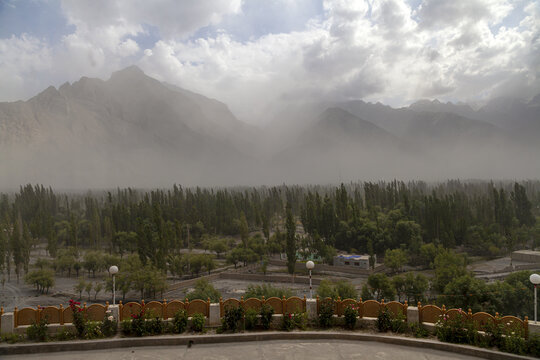 Aerial view of the Skardu valley landscape featuring lush green trees, towering hazy mountains in the background, and a decorative stone wall in the foreground in Skardu, Pakistan.