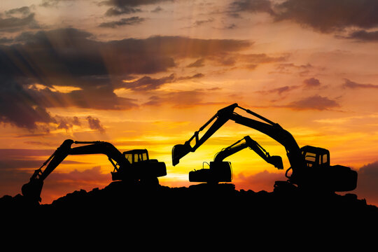 Three Crawler excavators silhouette are digging the soil in the construction site on   sunbeam  clouds  sky background .