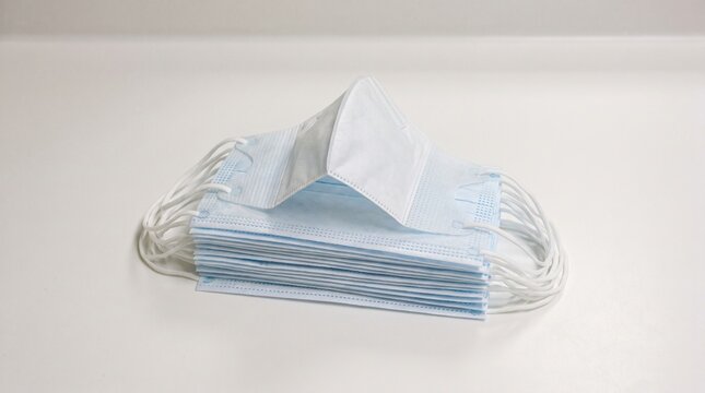 Stack of disposable surgical face masks on white surface