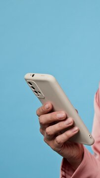 Vertical shot of Caucasian adult holding smartphone against blue background. Footage suits mobile application marketing, ecommerce campaigns, software tutorials, and user interface promotions