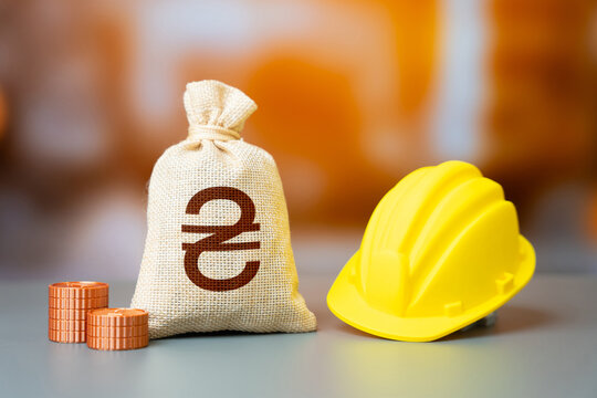 Ukrainian hryvnia money bag and a yellow construction worker's hard hat. Capital drives development. Urban growth and industrial expansion. Investments in real estate and infrastructure construction.