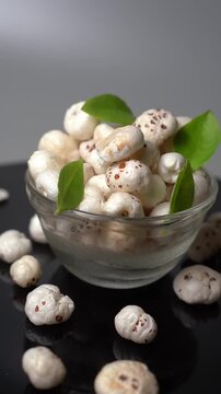 Fresh fox nuts or lotus seeds or Euryale ferox in a glass bowl with green leaves on dark surface, healthy organic vegetarian snack