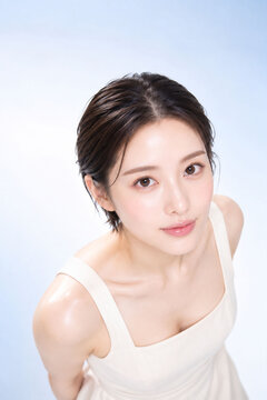 淡いブルー背景でカメラを見つめる若い日本人女性の透明感ある美容ポートレート