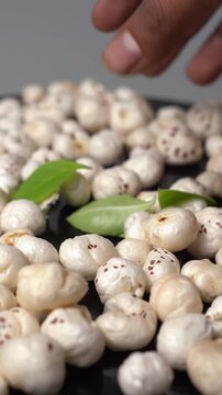 Prickly Water Lily or Euryale ferox seeds, known as makhana, arranged with green leaves on a dark surface for healthy snack display