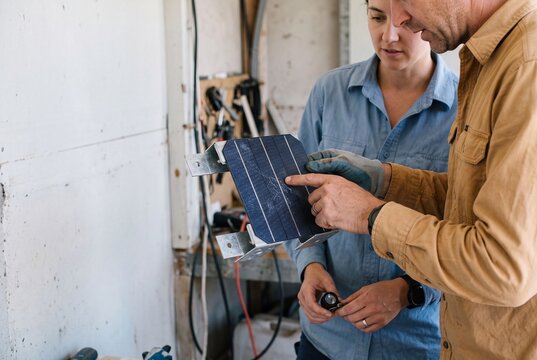 Two technicians inspecting and discussing a small solar panel prototype in a workshop