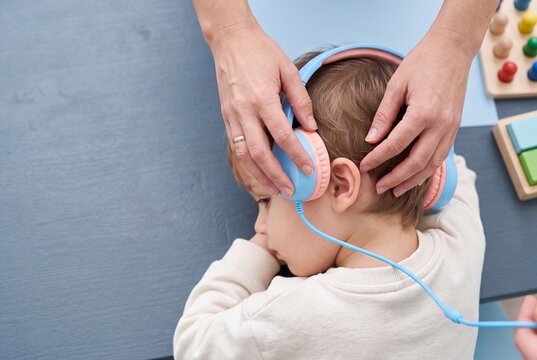 Hands of Specialist or Mother Putting Headphones on Toddler Boy During Hearing Test