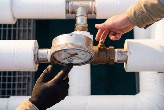 Industrial technicians inspect and adjust an outdoor pipeline system with a dial pressure gauge and control valve