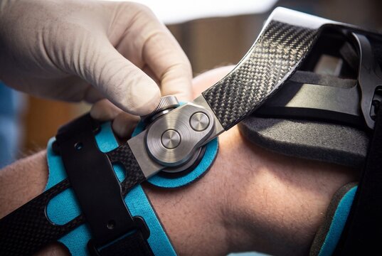 Doctor adjusting a modern carbon fiber orthopedic knee brace on a patient during rehabilitation treatment