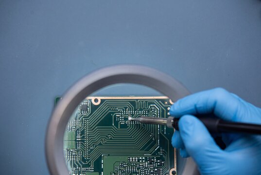 Technician soldering circuit board under magnifying glass in electronics repair workshop