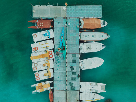 Aerial view of Lago Castreccioni with a floating dock surrounded by moored pedalos, kayaks, and small motorboats on turquoise water in Cingoli, Marche, Italy.