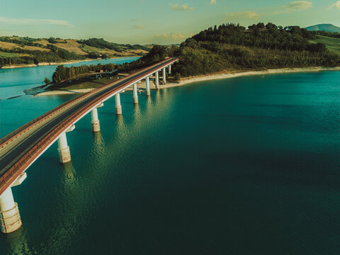 Aerial view of the bridge crossing Lago Castreccioni, surrounded by rolling hills and lush greenery, Cingoli, Marche, Italy.