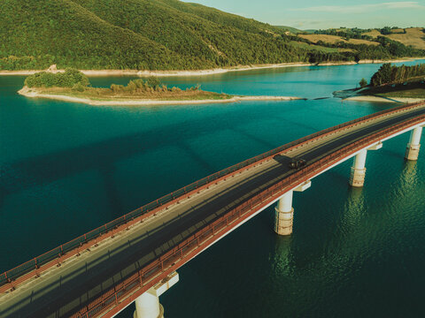 Aerial view of the bridge crossing Lago Castreccioni surrounded by lush green hills and clear blue water in Cingoli, Marche, Italy.