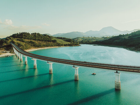 Aerial view of the bridge crossing Lago Castreccioni with surrounding green hills and calm turquoise water in Cingoli, Marche, Italy.