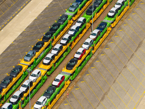 Aerial view of a large vehicle transport and storage facility with rows of new cars loaded onto train carriages parked on tracks in Poland.